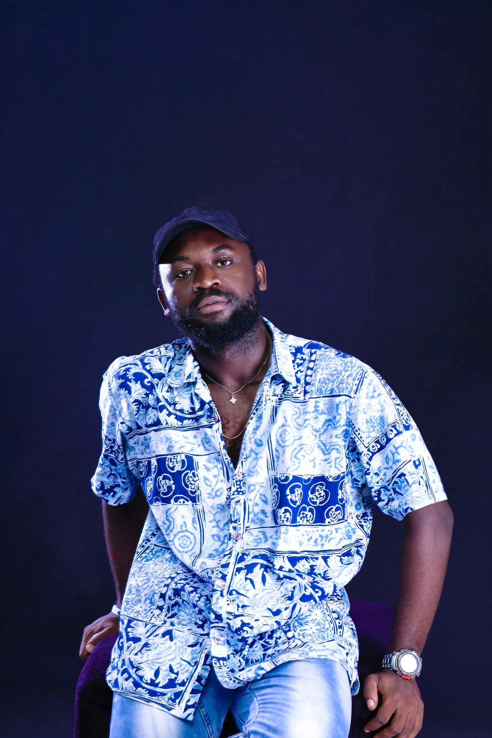 Studio portrait of a bearded man in a blue patterned shirt, seated and looking at the camera.
